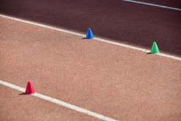 Sportwissenschaft – je ein roter, grüner und blauer Kegel stehen auf der weissen Linie der Tartanbahn.