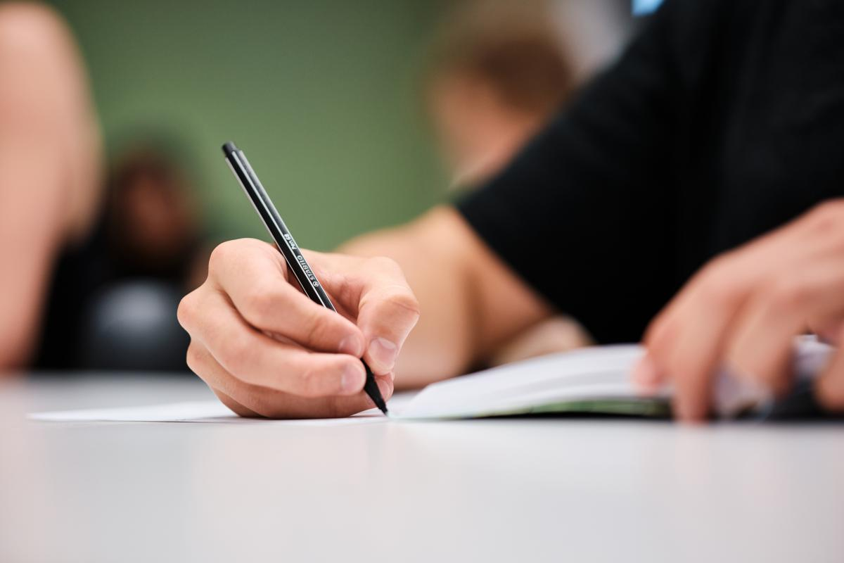 Person hält einen Stift in der Hand und schreibt auf ein Blatt Papier.