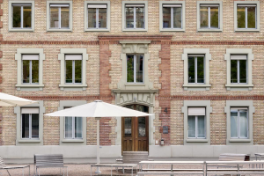 Uni Engehaldenstrasse 4 – Aussenbereich – Sitzbänke, Tische, Sonnenschirme im Vordergrund.