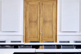 H6 – Sitzungszimmer 101 – Eingangstüre mit Tischen und schwarzen Sesseln im Vordergrund.