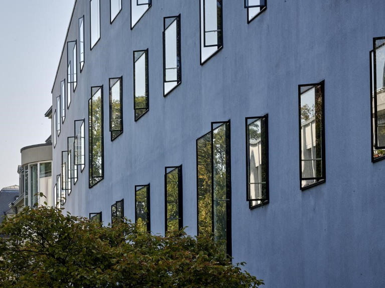 UniS Rückfront mit zum Teil geöffneten Fenstern – grüner Busch im Vordergrund – bei Sonnenschein