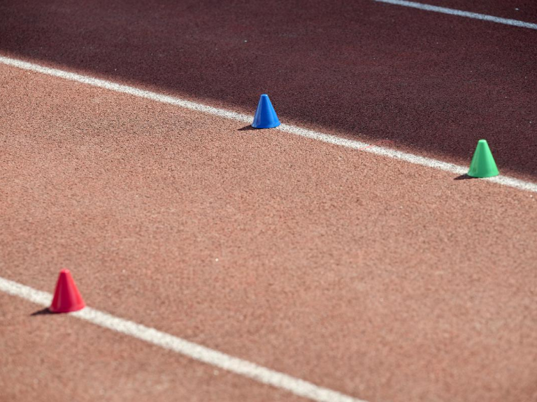 Sportwissenschaft – je ein roter, grüner und blauer Kegel stehen auf der weissen Linie der Tartanbahn.